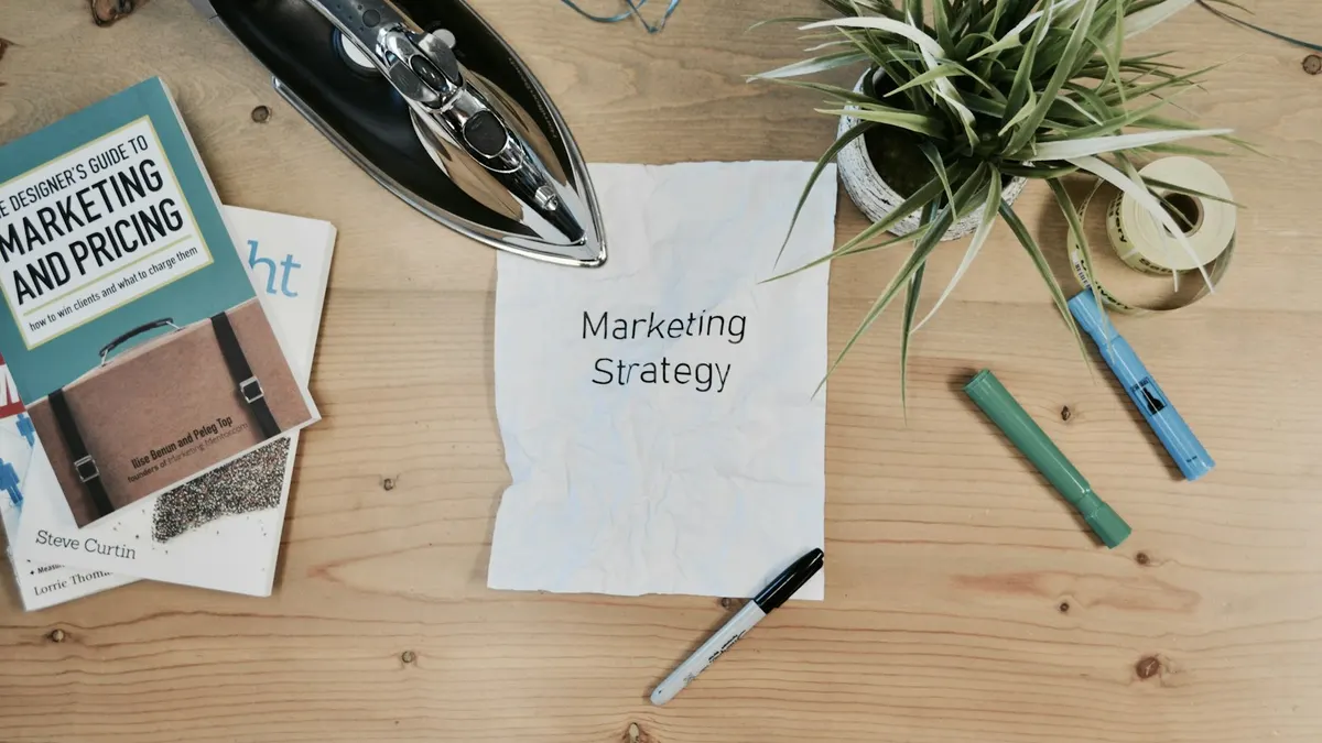 A handwritten note reading 'Marketing Strategy' on a desk surrounded by marketing books and supplies