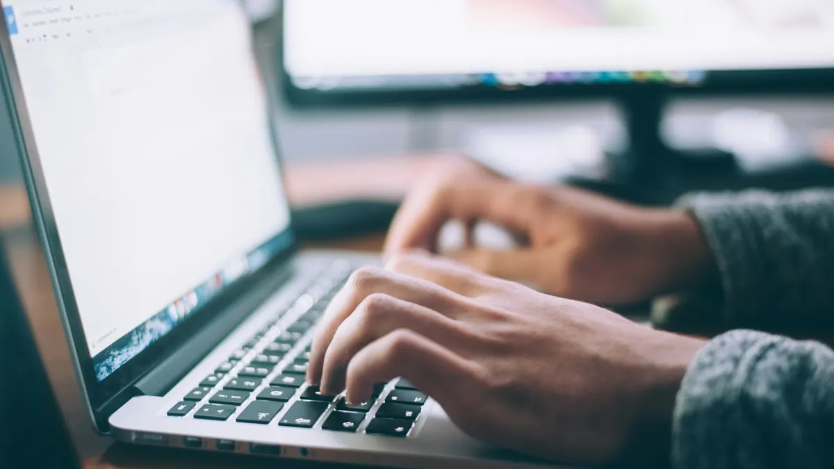 Close-up of a person's hands typing on a laptop keyboard while drafting a document